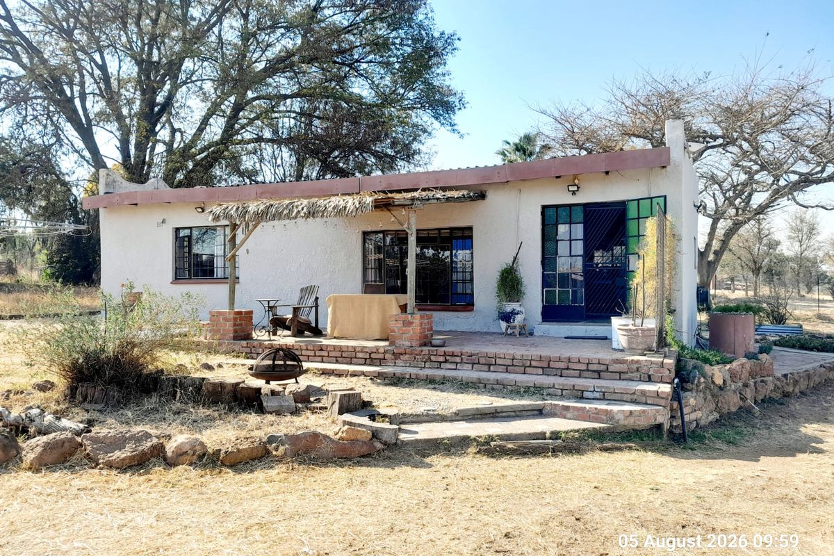 Rear view of a farm cottage featuring a brick patio, thatched pergola, and established garden surroundings.
