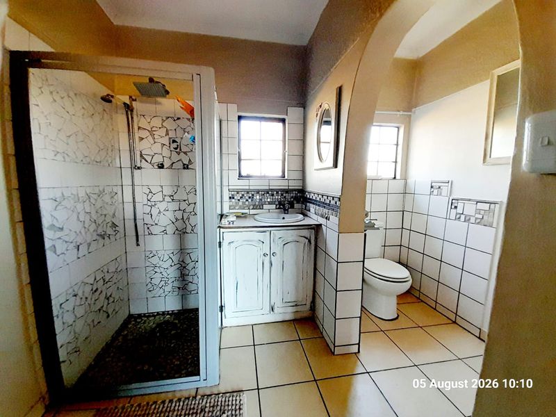 A functional bathroom featuring a shower enclosure, vanity cabinet with basin, and toilet, finished with tiled walls and flooring.