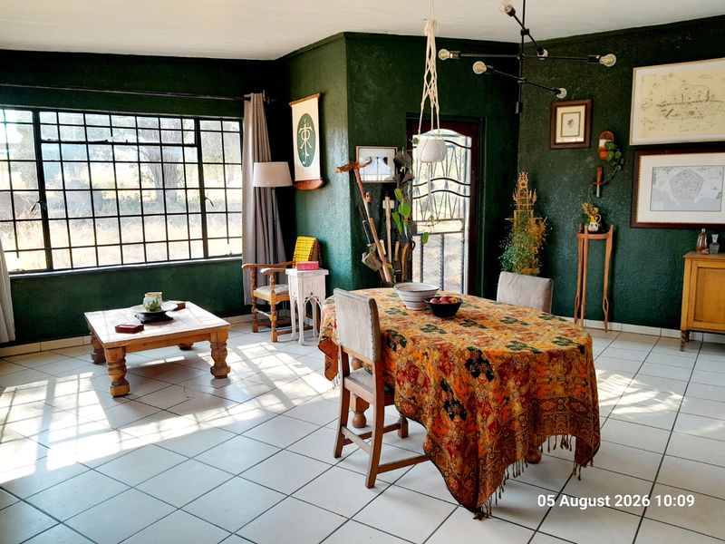 Spacious open-plan living and dining area featuring tiled flooring, large steel-framed windows, and a distinctive dark green textured wall finish.
