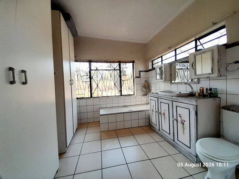 A dated bathroom featuring a tiled bathtub, built-in vanity with storage, and floor-to-ceiling cupboards, requiring cosmetic updates to modernize the space.