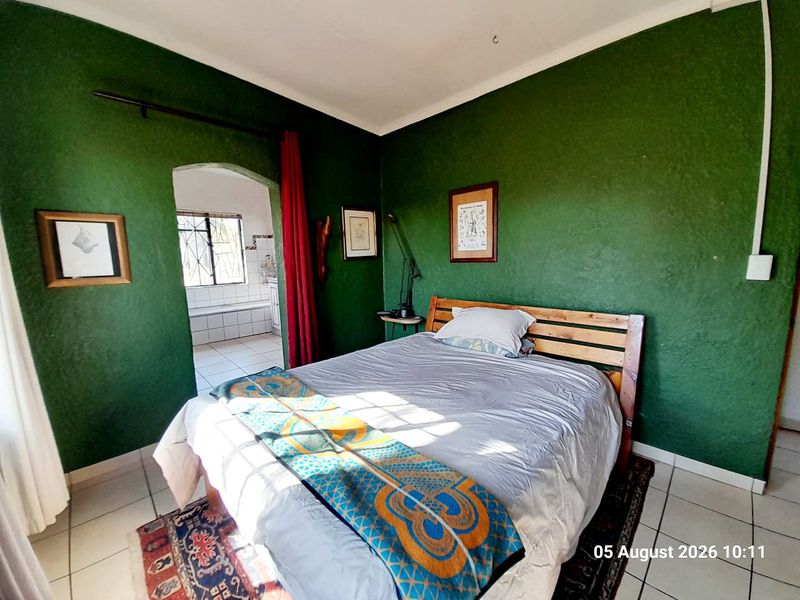 A bedroom featuring tiled flooring and an arched doorway leading to an adjoining bathroom, with green textured walls.