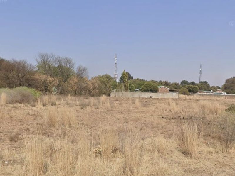 A view of a vacant residential plot featuring dry grass and a boundary wall in the background.