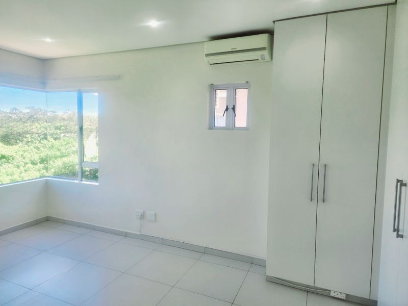 A bright, empty bedroom featuring tiled flooring, a built-in wardrobe, and a split-system air conditioner with a pleasant corner window view.