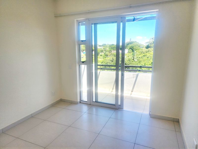 A bright, empty bedroom featuring neutral tiled flooring and a sliding glass door providing direct access to a private balcony.