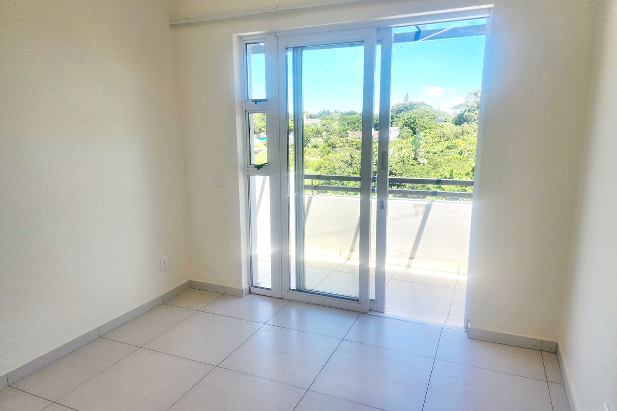 A bright, empty bedroom featuring neutral tiled flooring and a sliding glass door providing direct access to a private balcony.