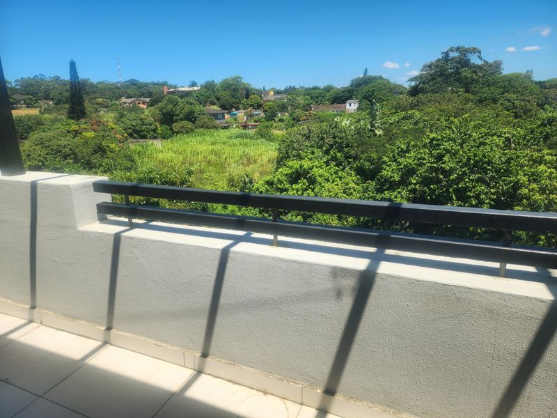 A clean, open balcony featuring tiled flooring and a modern metal balustrade, offering an elevated view over the surrounding greenery.