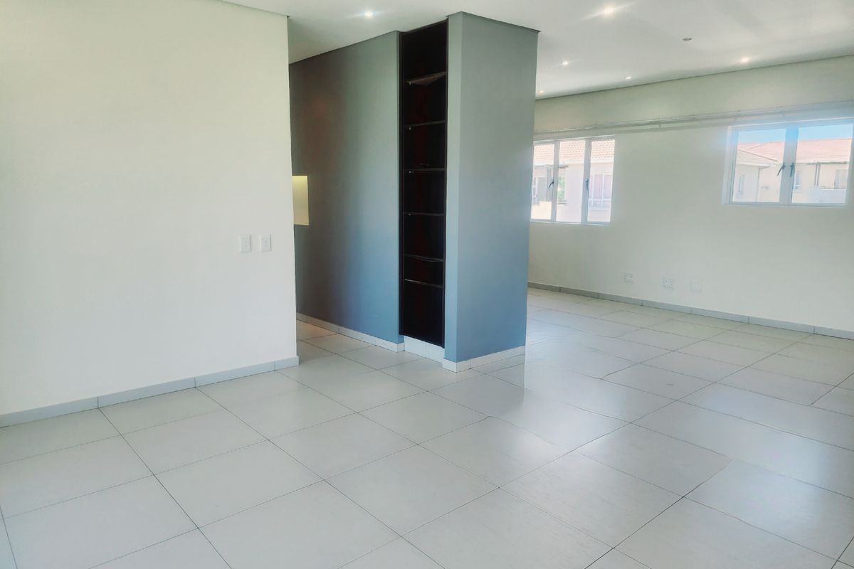 A bright, open-plan living area featuring neutral tiled flooring, recessed downlighting, and a modern built-in shelving unit, offering a versatile and spacious layout.
