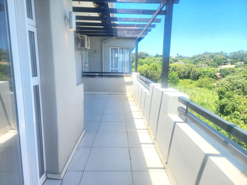 Spacious balcony featuring tiled flooring, a timber pergola, and metal balustrades, offering an open outdoor area with scenic green views.