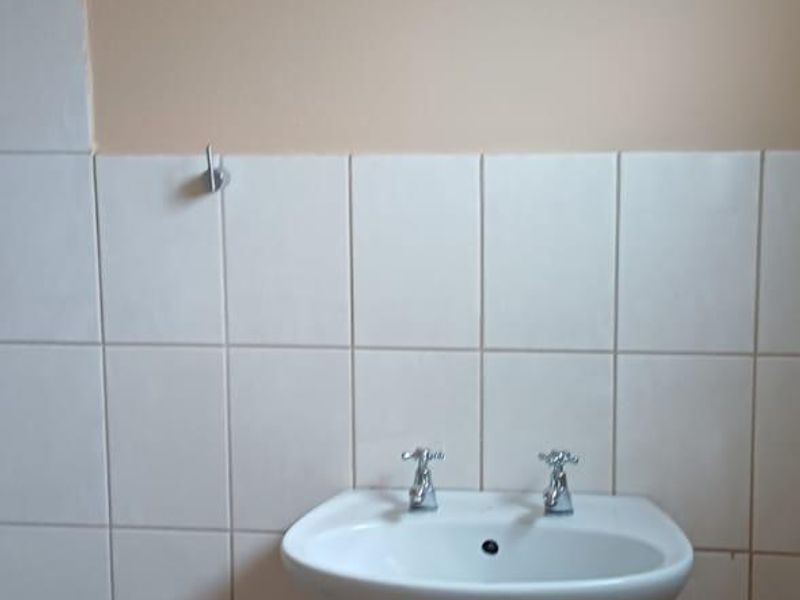 A simple bathroom featuring a white pedestal basin with chrome taps and a tiled splashback.