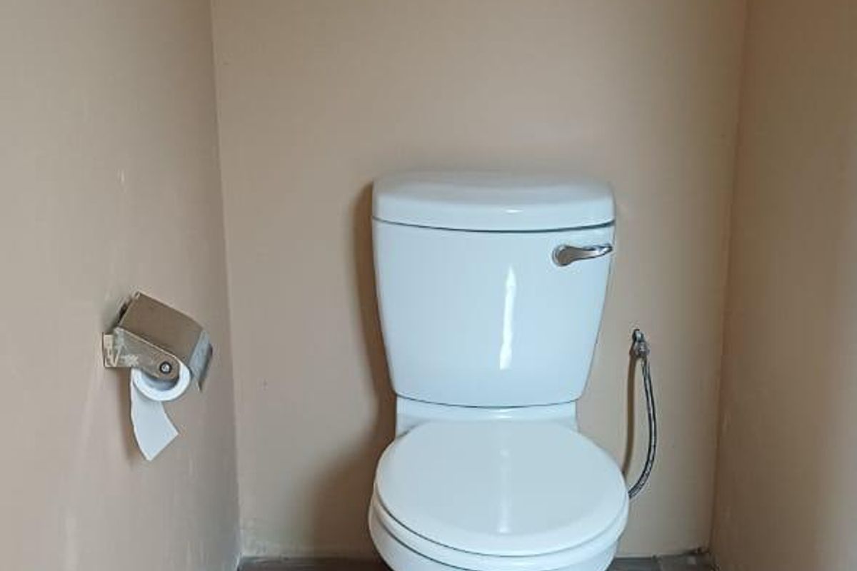 A small, functional bathroom featuring a white toilet, bidet spray, and wood-look tiled flooring.