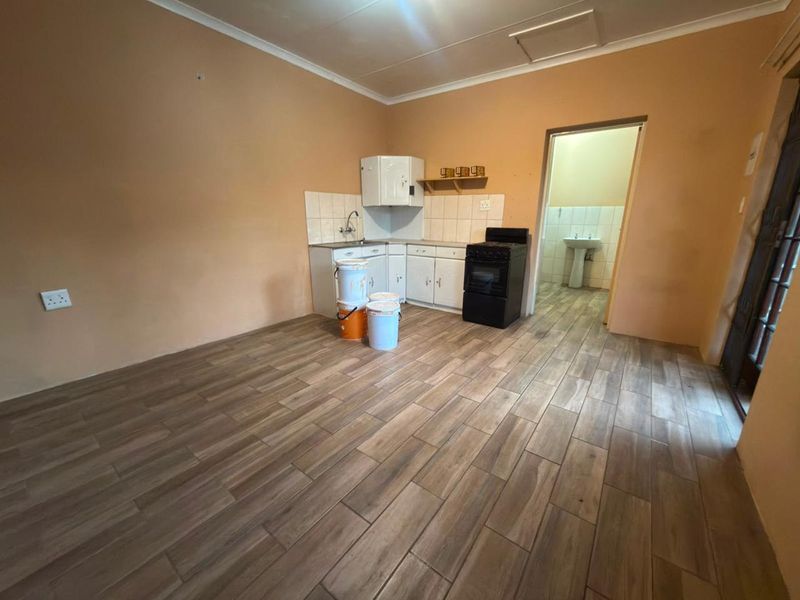 A compact kitchen area featuring wood-look floor tiles, basic cabinetry, and a freestanding stove, with an adjacent view into a bathroom space.