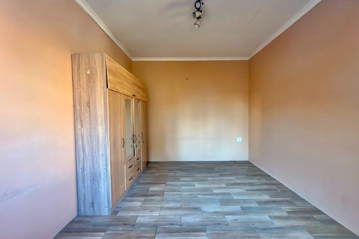 A bedroom featuring wood-look tiled flooring, a built-in wardrobe with mirrored panels, and neutral wall tones.