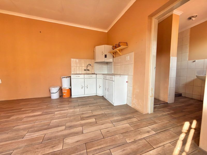 A compact kitchen area featuring basic cabinetry, a sink, tiled splashbacks, and wood-look floor tiles, currently in need of cosmetic updates.