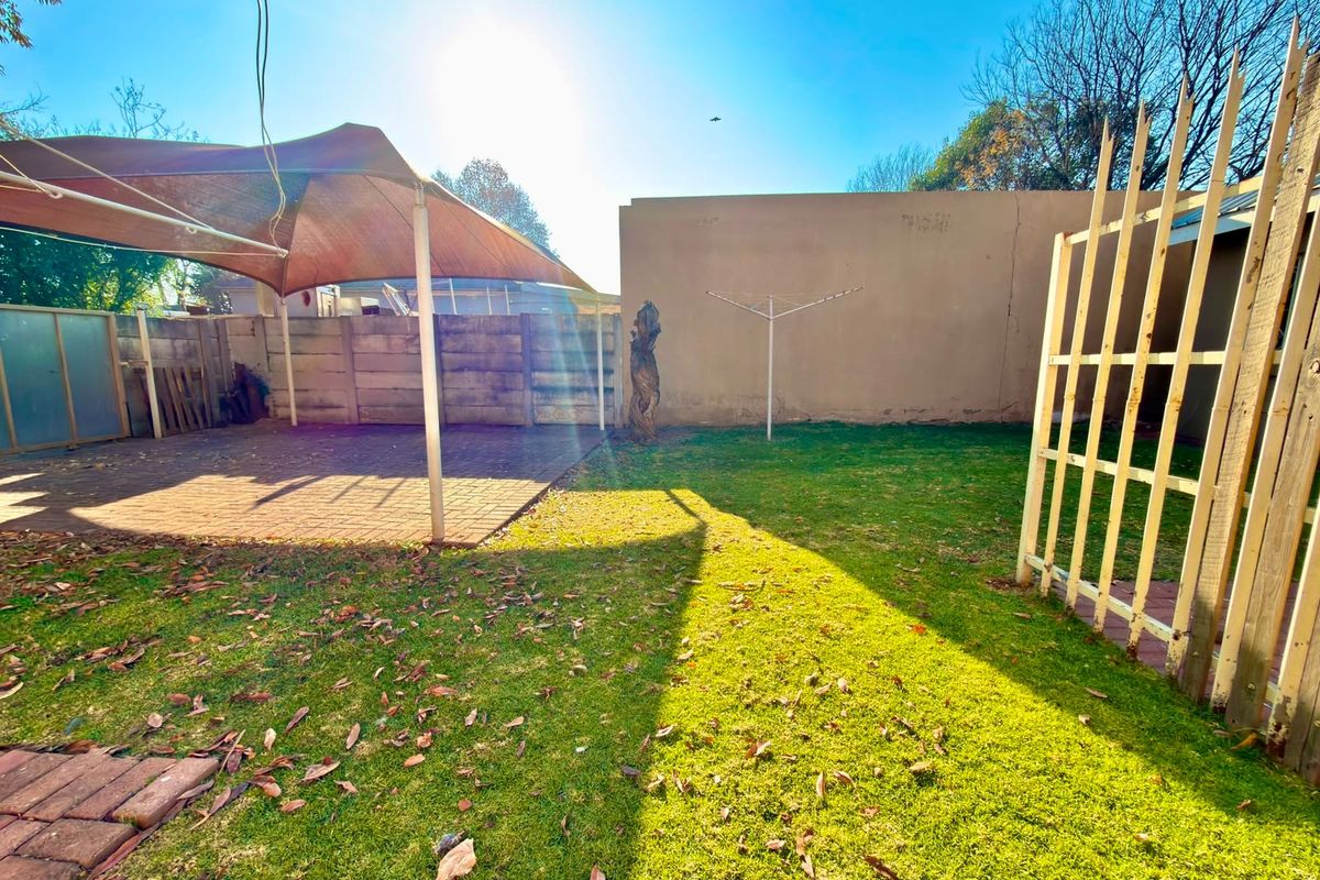 Rear garden area featuring a paved patio with a shade sail, lawn space, and a boundary wall.