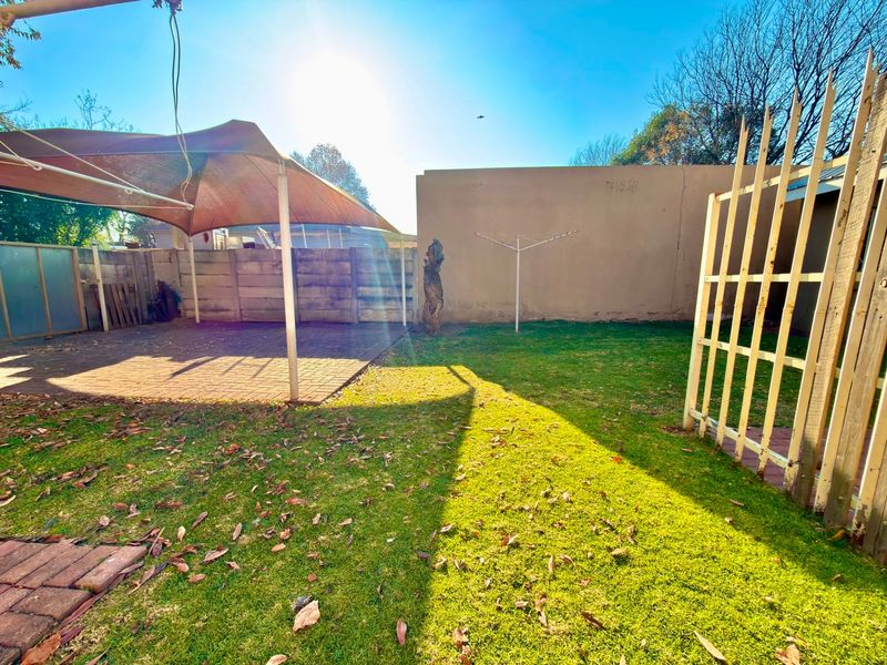 Rear garden area featuring a paved patio with a shade sail, lawn space, and a boundary wall.