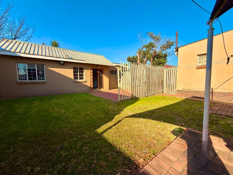 Rear view of the cottage featuring a paved patio area, lawn, and secure perimeter fencing.