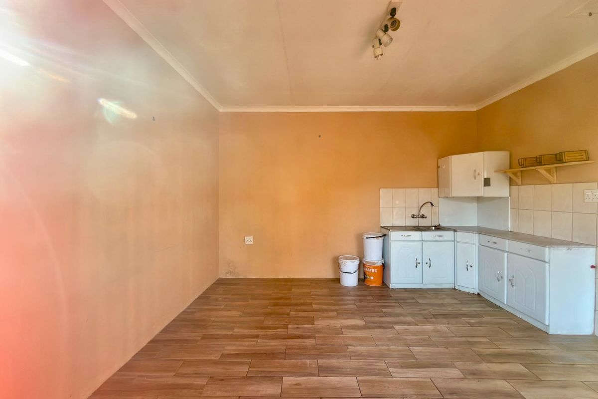 A compact, empty kitchen area featuring wood-look floor tiles, basic cabinetry, a stainless steel sink, and a tiled backsplash.