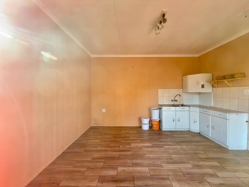 A compact, empty kitchen area featuring wood-look floor tiles, basic cabinetry, a stainless steel sink, and a tiled backsplash.