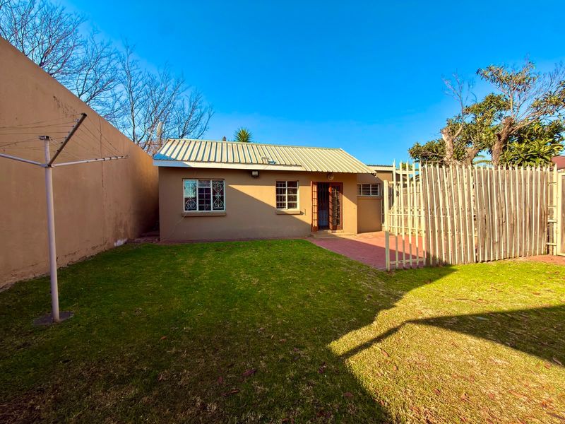 Rear view of the cottage featuring a paved patio area, a private lawn, and secure boundary fencing.