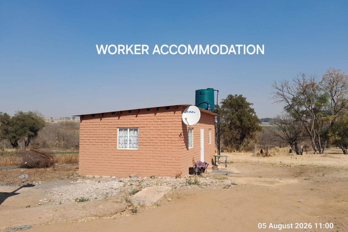 A detached brick worker accommodation unit featuring a roof-mounted water storage tank and satellite dish, situated on a rural farm property.