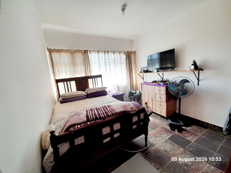 A functional bedroom featuring tiled flooring and large windows with curtain rails, providing a simple and practical living space.