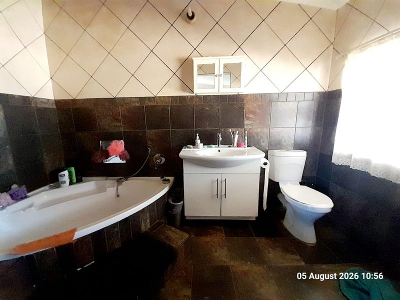 A functional bathroom featuring a corner bathtub, vanity cabinet with basin, and toilet, finished with dark wall and floor tiling.