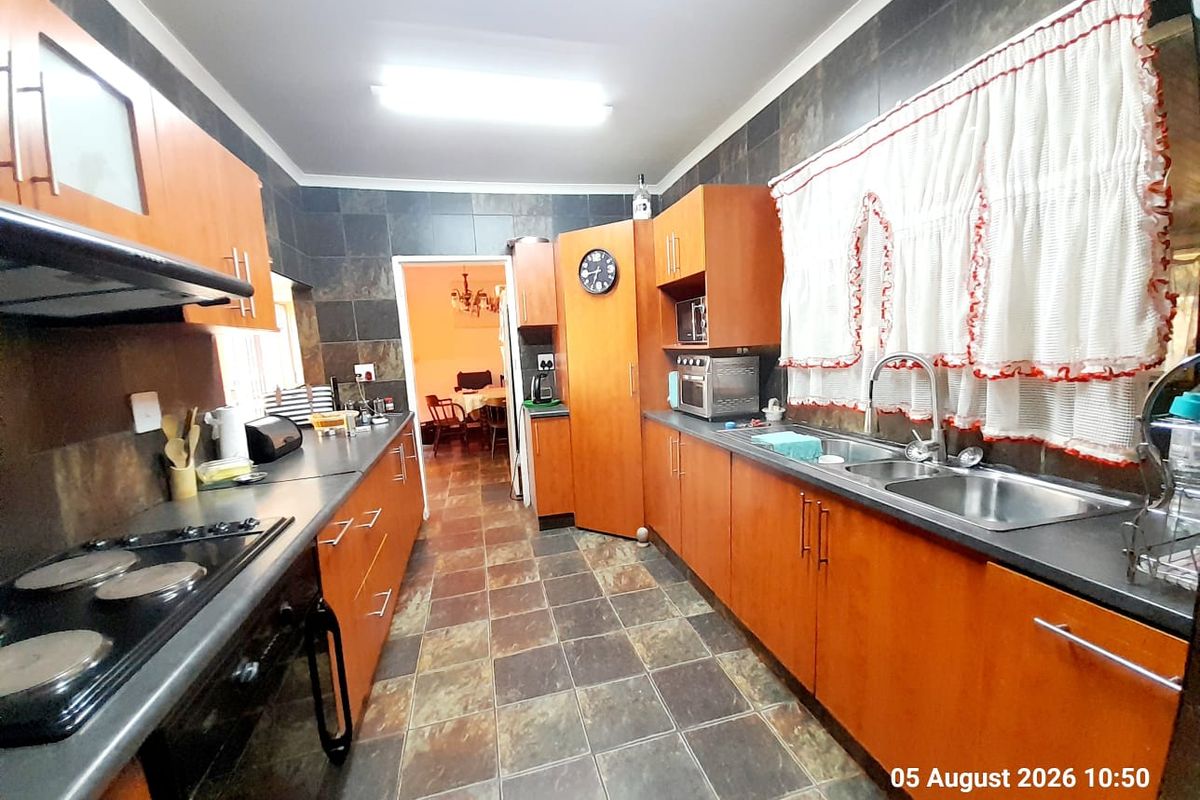A functional kitchen featuring wooden cabinetry, dark tiled splashbacks, a double basin sink, and an integrated electric hob with an extractor fan.