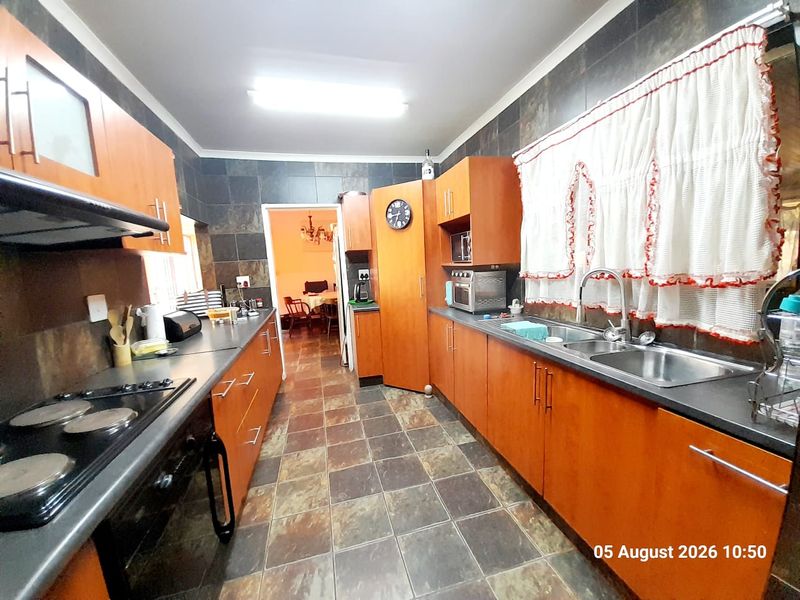 A functional kitchen featuring wooden cabinetry, dark tiled splashbacks, a double basin sink, and an integrated electric hob with an extractor fan.