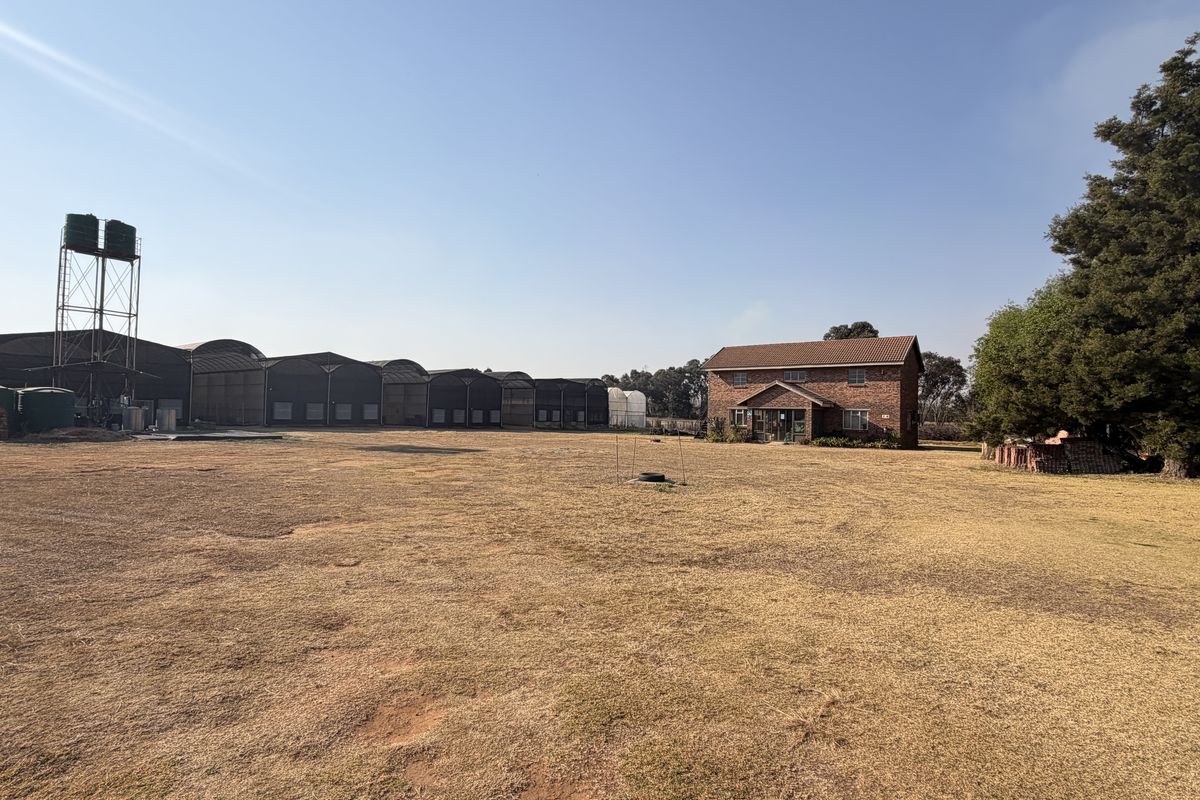 Expansive small holding property featuring a brick residential dwelling, large agricultural storage sheds, and elevated water storage infrastructure on a spacious plot.