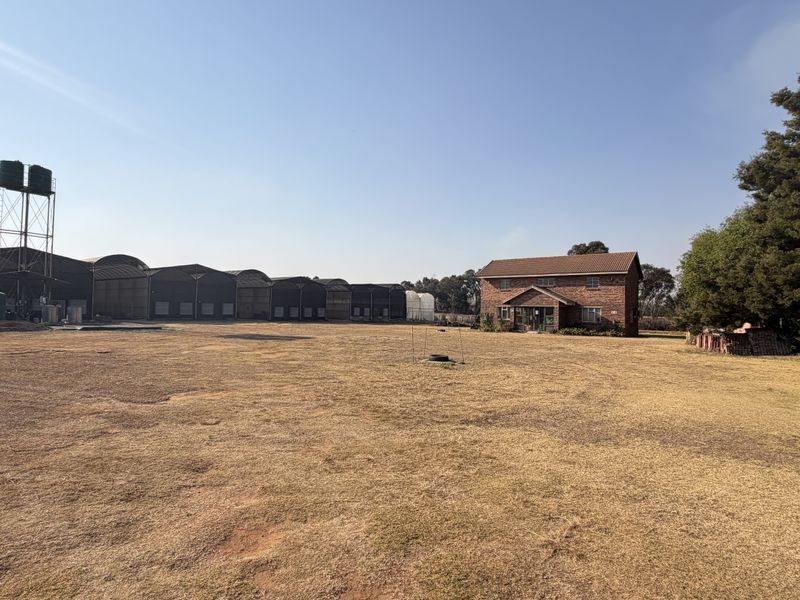 Expansive small holding property featuring a brick residential dwelling, large agricultural storage sheds, and elevated water storage infrastructure on a spacious plot.