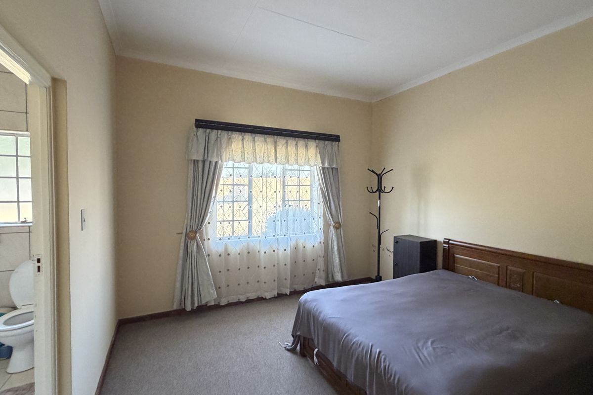 A standard bedroom featuring carpeted flooring, security bars on the window, and an en-suite bathroom access.