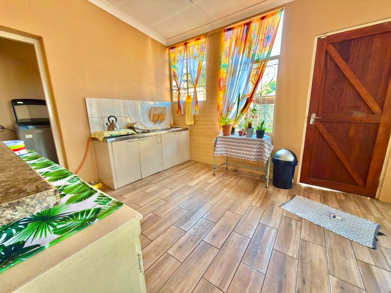 A functional scullery area featuring tiled flooring, a stainless steel sink with splashback, and direct access to the exterior via a timber door.