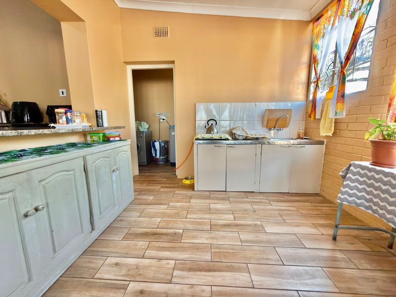 A functional kitchen area featuring tiled flooring, built-in cabinetry, a stainless steel sink, and a granite countertop, with an adjacent utility space.