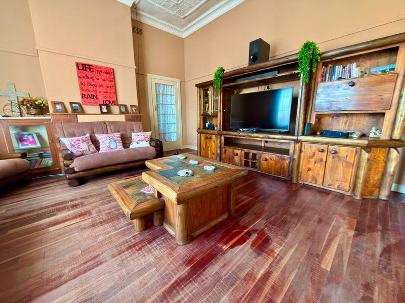 Spacious living room featuring original hardwood flooring, ornate ceiling detailing, and a substantial built-in timber entertainment unit with a brick fireplace surround.
