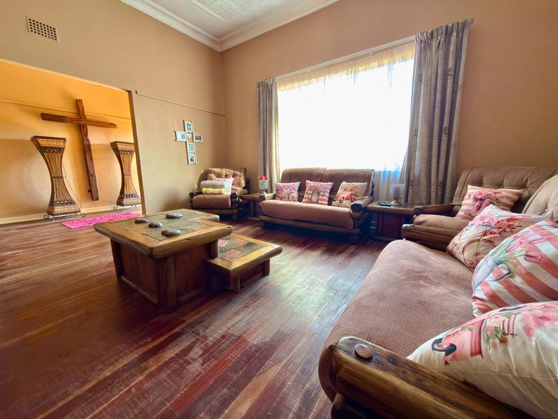 A spacious living room featuring original hardwood flooring, ornate ceiling cornicing, and a large window allowing for ample natural light.