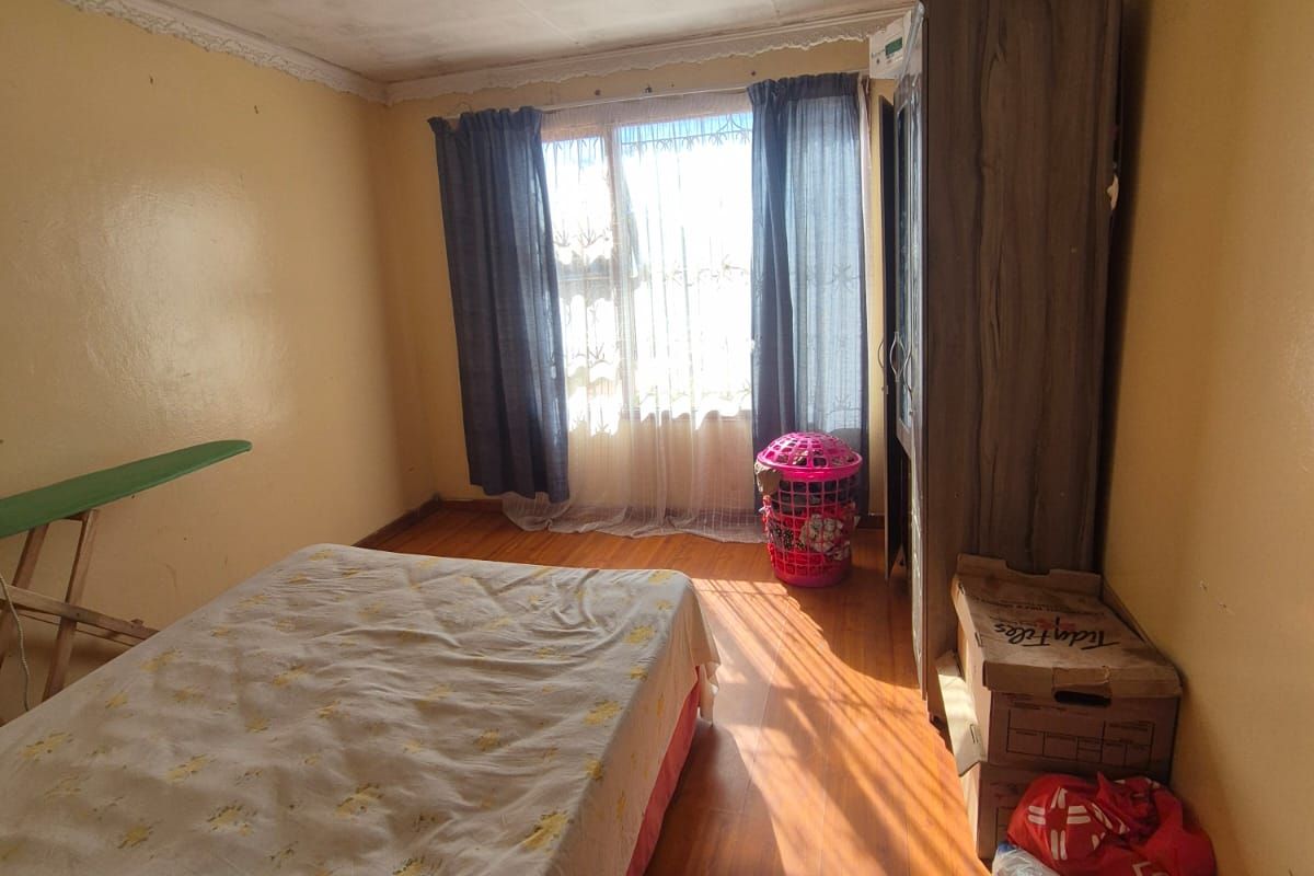 A bedroom featuring laminate flooring, a ceiling rose, and decorative cornice. The room requires cosmetic updates to the walls and ceiling.