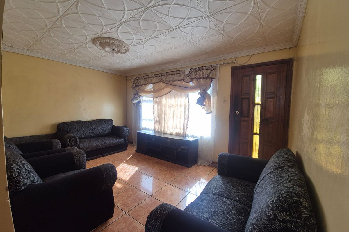 A living room featuring tiled flooring, a decorative ceiling with a central rose, and a timber entrance door with glass panels.