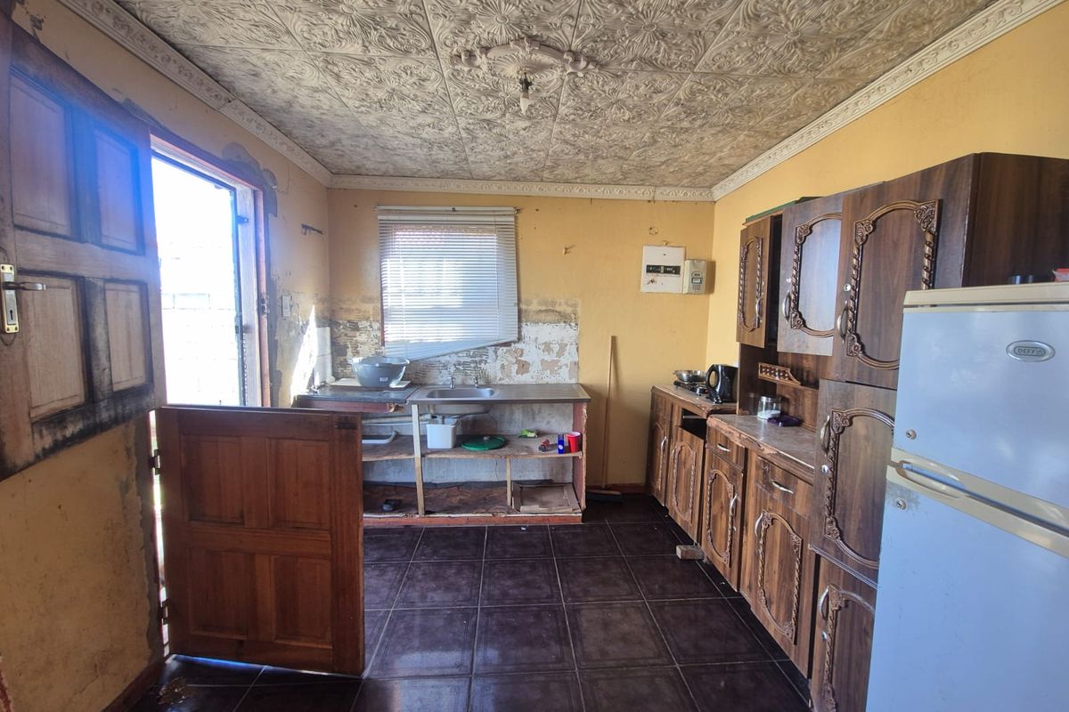 A dated kitchen featuring ornate pressed metal ceilings, dark tiled flooring, and traditional wooden cabinetry requiring significant renovation and cosmetic updates.
