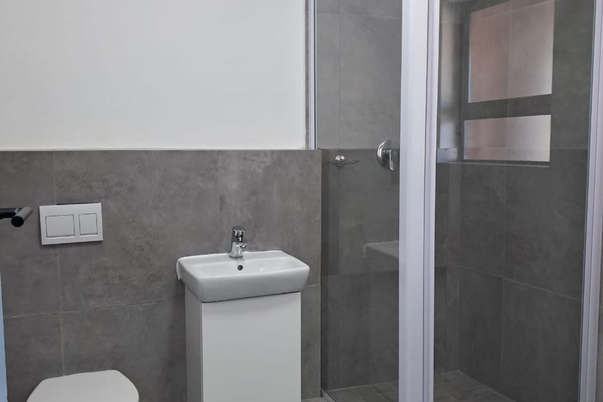 Modern bathroom featuring a wall-mounted toilet, vanity basin, and a glass-enclosed shower with contemporary grey tiling throughout.
