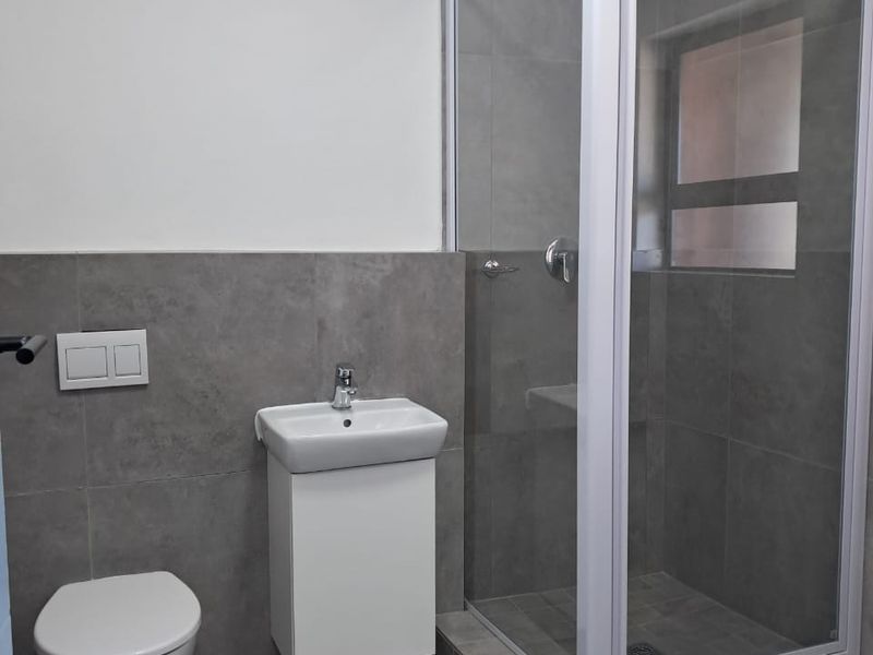 Modern bathroom featuring a wall-mounted toilet, vanity basin, and a glass-enclosed shower with contemporary grey tiling throughout.