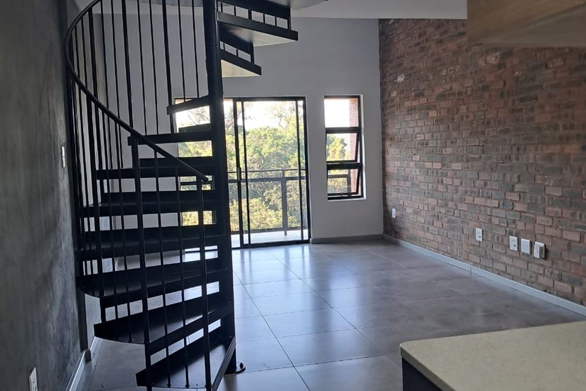 Open-plan living area featuring a modern black spiral staircase, exposed brick feature wall, large format floor tiles, and access to a balcony.