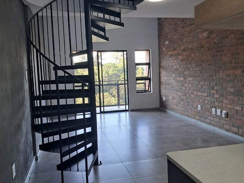 Open-plan living area featuring a modern black spiral staircase, exposed brick feature wall, large format floor tiles, and access to a balcony.