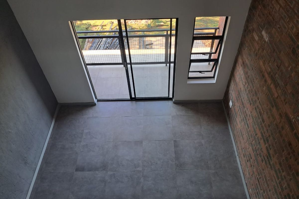 An empty living area featuring modern tiled floors, an exposed brick feature wall, and direct access to a balcony through sliding glass doors.