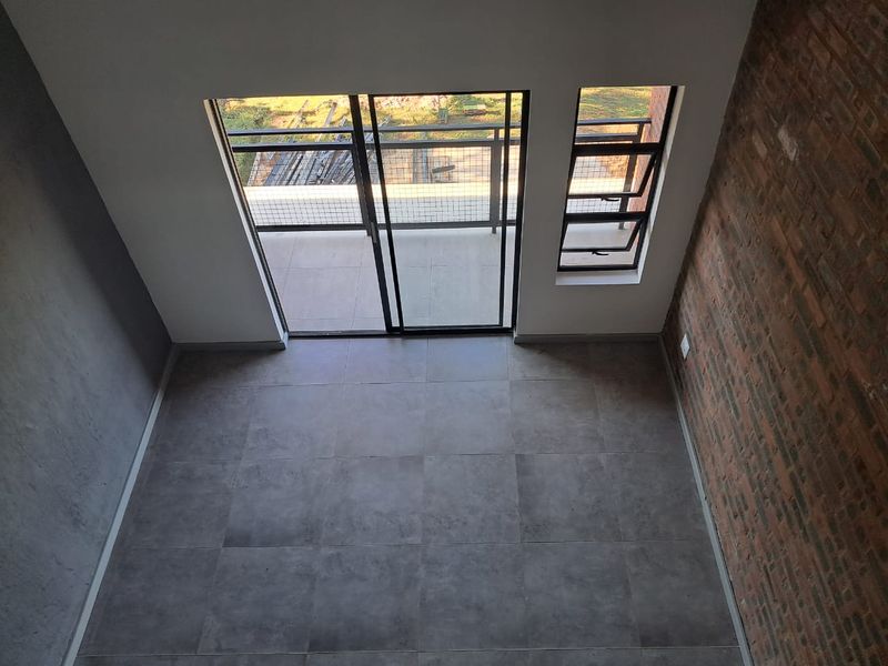 An empty living area featuring modern tiled floors, an exposed brick feature wall, and direct access to a balcony through sliding glass doors.