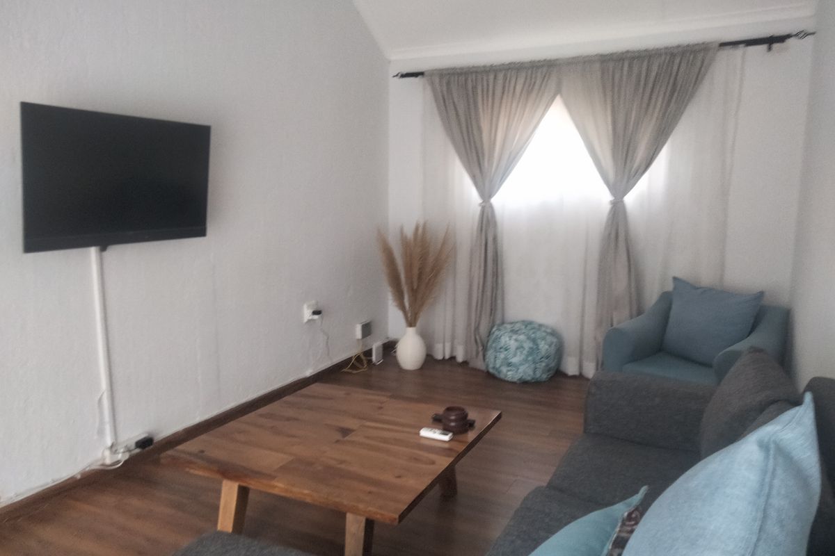 A cozy living room featuring laminate flooring, a wall-mounted television with cable trunking, and window curtains.