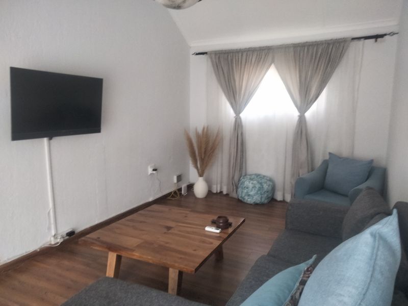 A cozy living room featuring laminate flooring, a wall-mounted television with cable trunking, and window curtains.