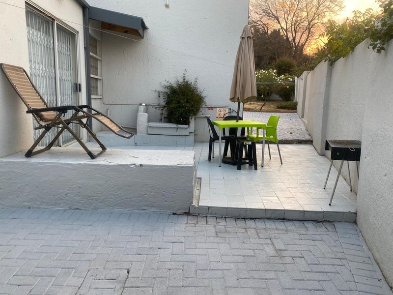 A paved outdoor patio area featuring a raised concrete platform, sliding door access, and perimeter boundary walls, suitable for outdoor dining and relaxation.