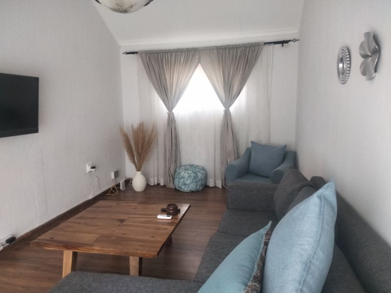 A cozy living room featuring laminate flooring, a vaulted ceiling, and a window dressed with curtains.