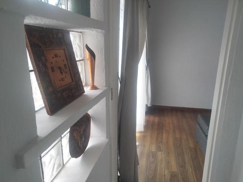 A hallway featuring built-in shelving with decorative glass block inserts and wood-look laminate flooring, leading into an adjacent living space.
