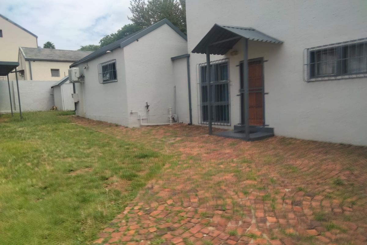Rear exterior view of the property featuring a brick paved patio area, security bars on windows, and a small metal entrance awning.